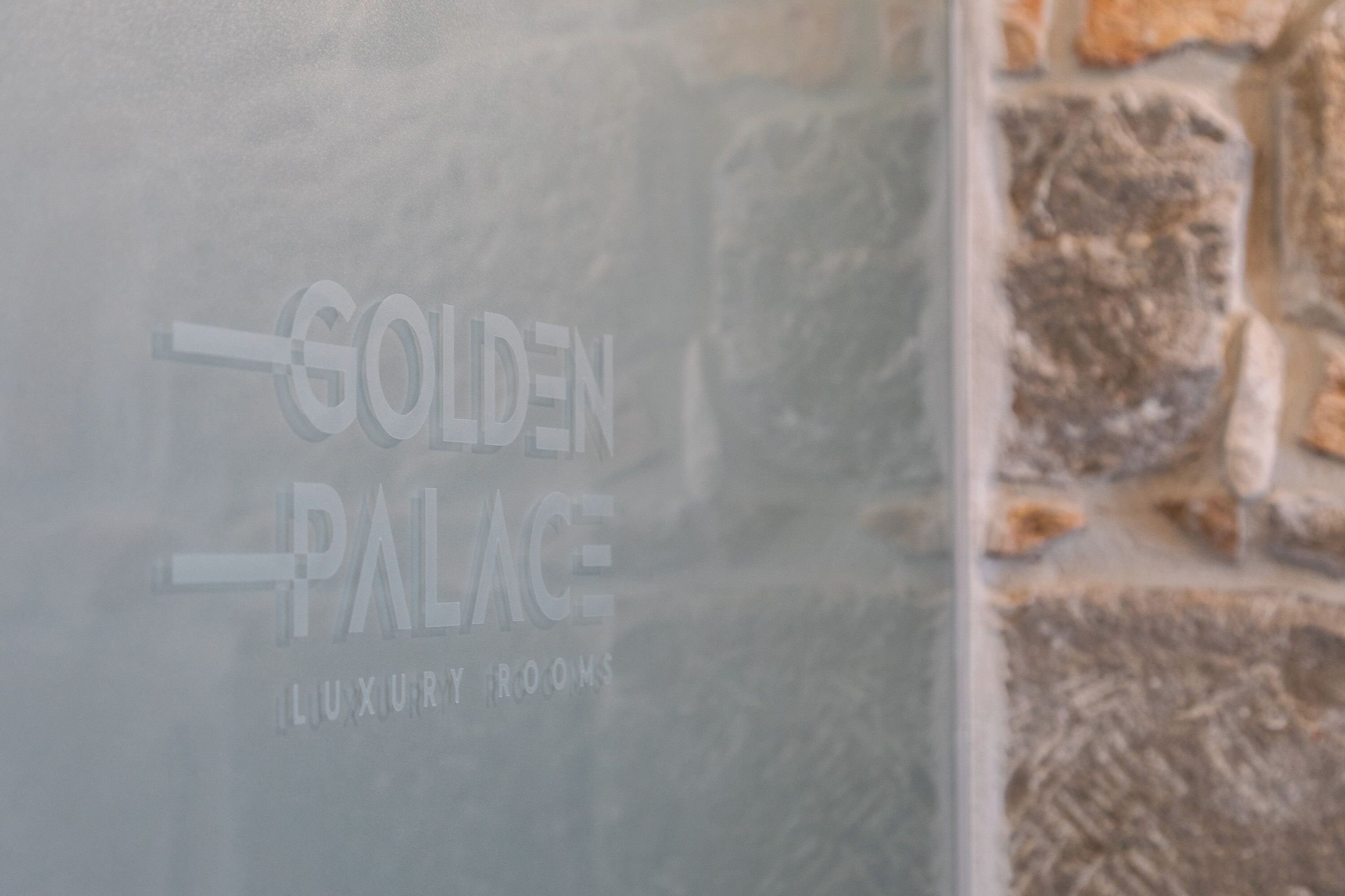 A sign with the text "GOLDEN PALACE LUXURY ROOMS" on a glass surface.