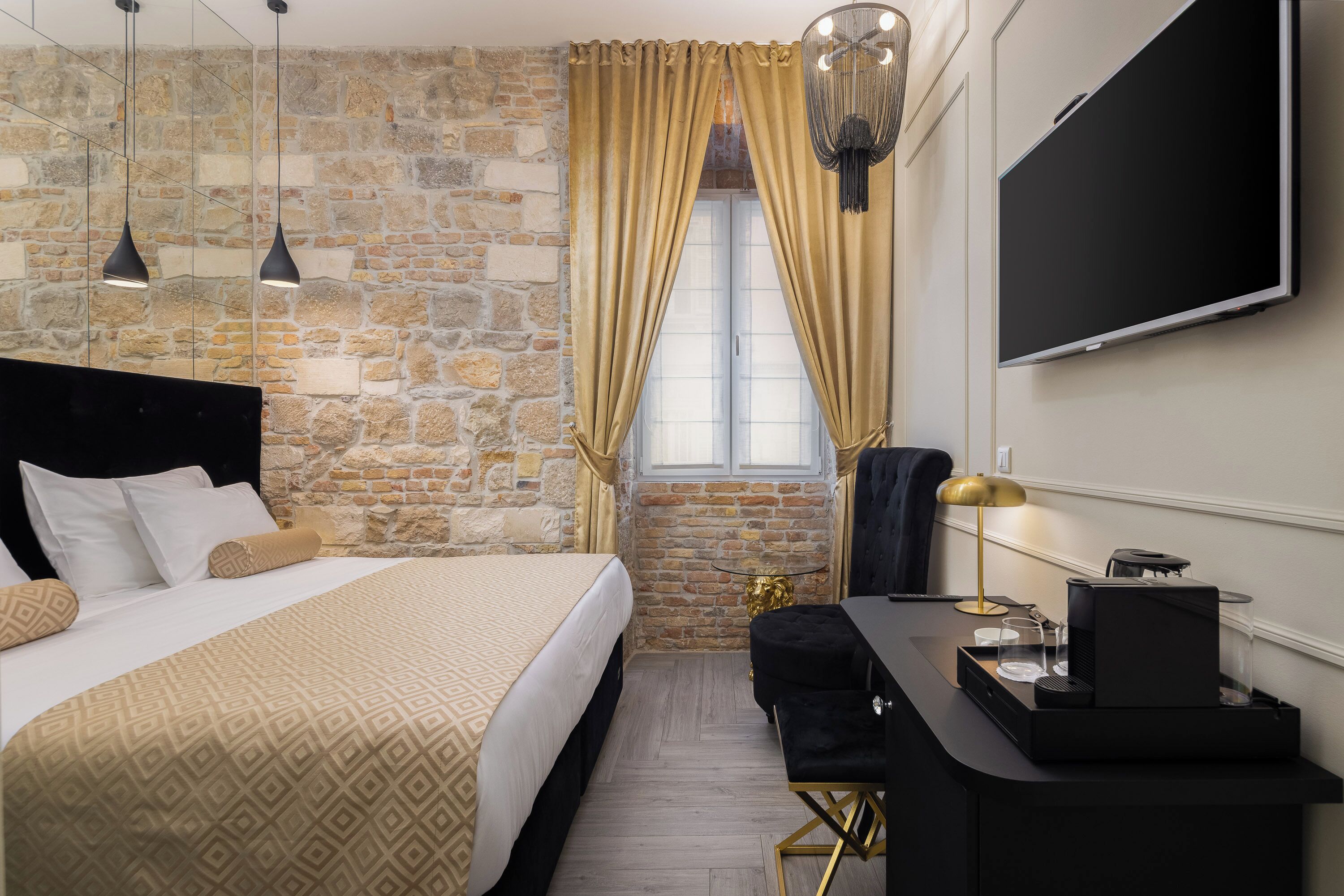 Una habitación de hotel con pared de piedra, una cama con ropa de cama estampada, un escritorio con cafetera y un televisor montado en la pared.