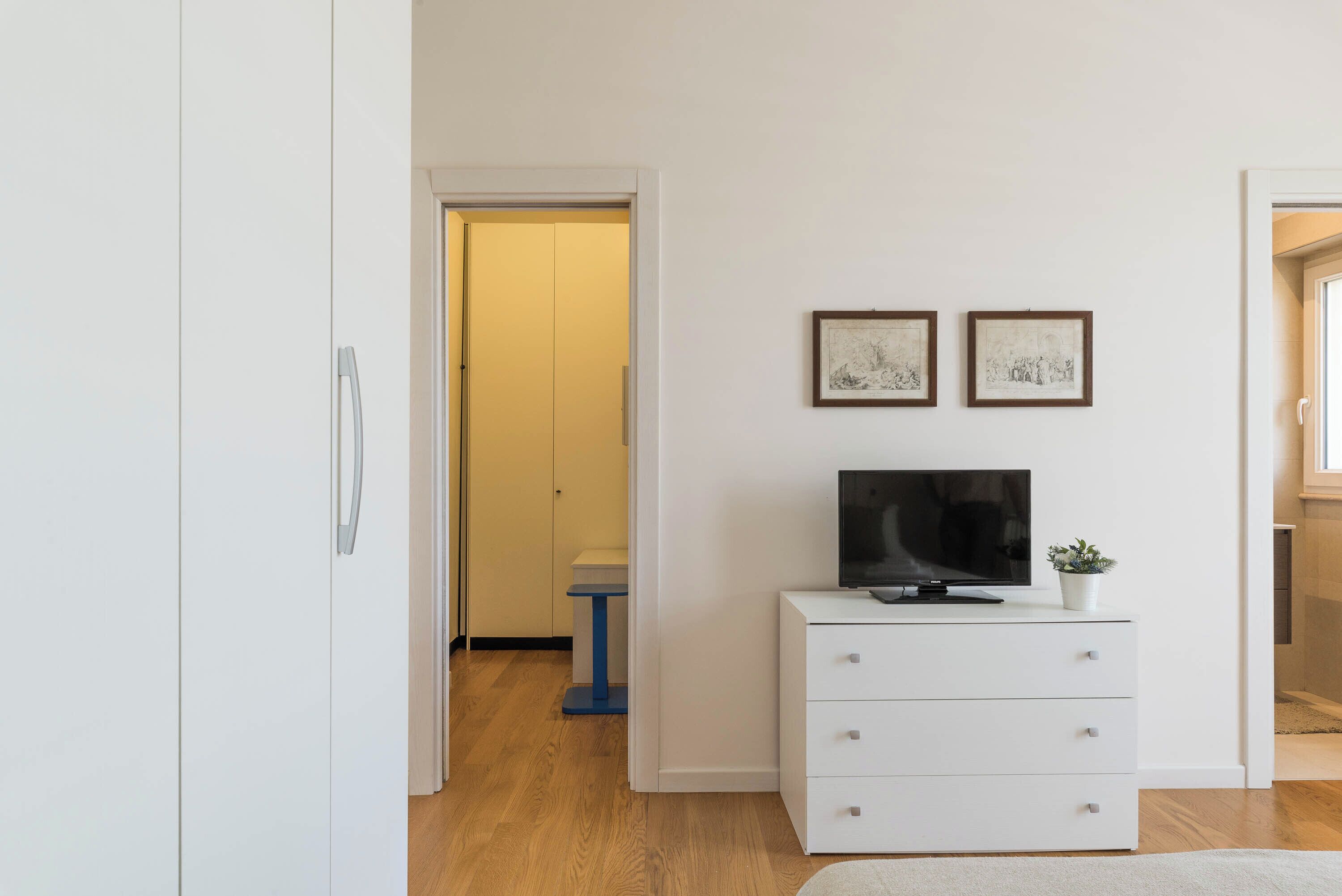 A modern room with a white dresser, a flat-screen TV, and two framed pictures on the wall.