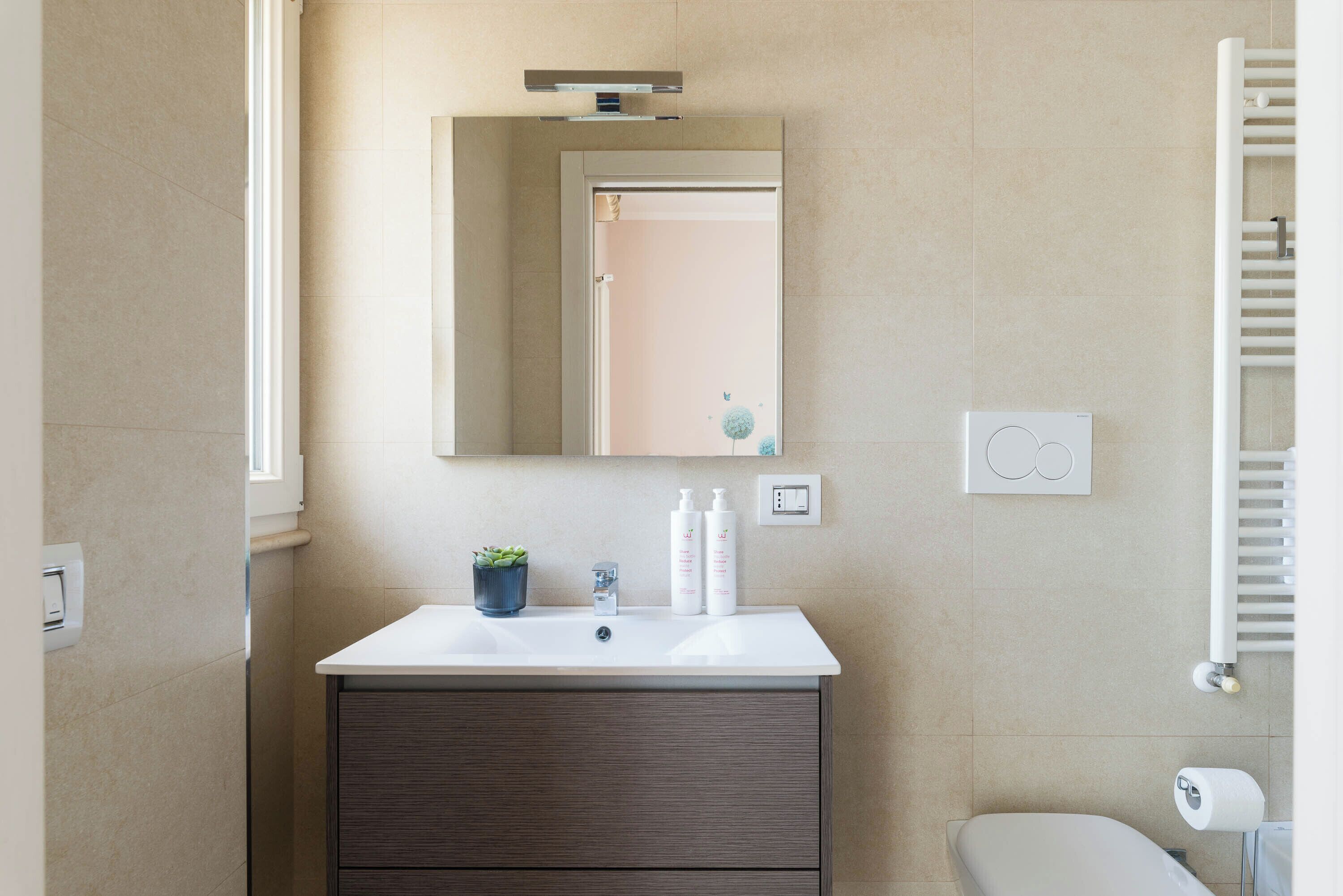 A bathroom with a white sink, dark wooden cabinet, a mirror, and a towel rack.