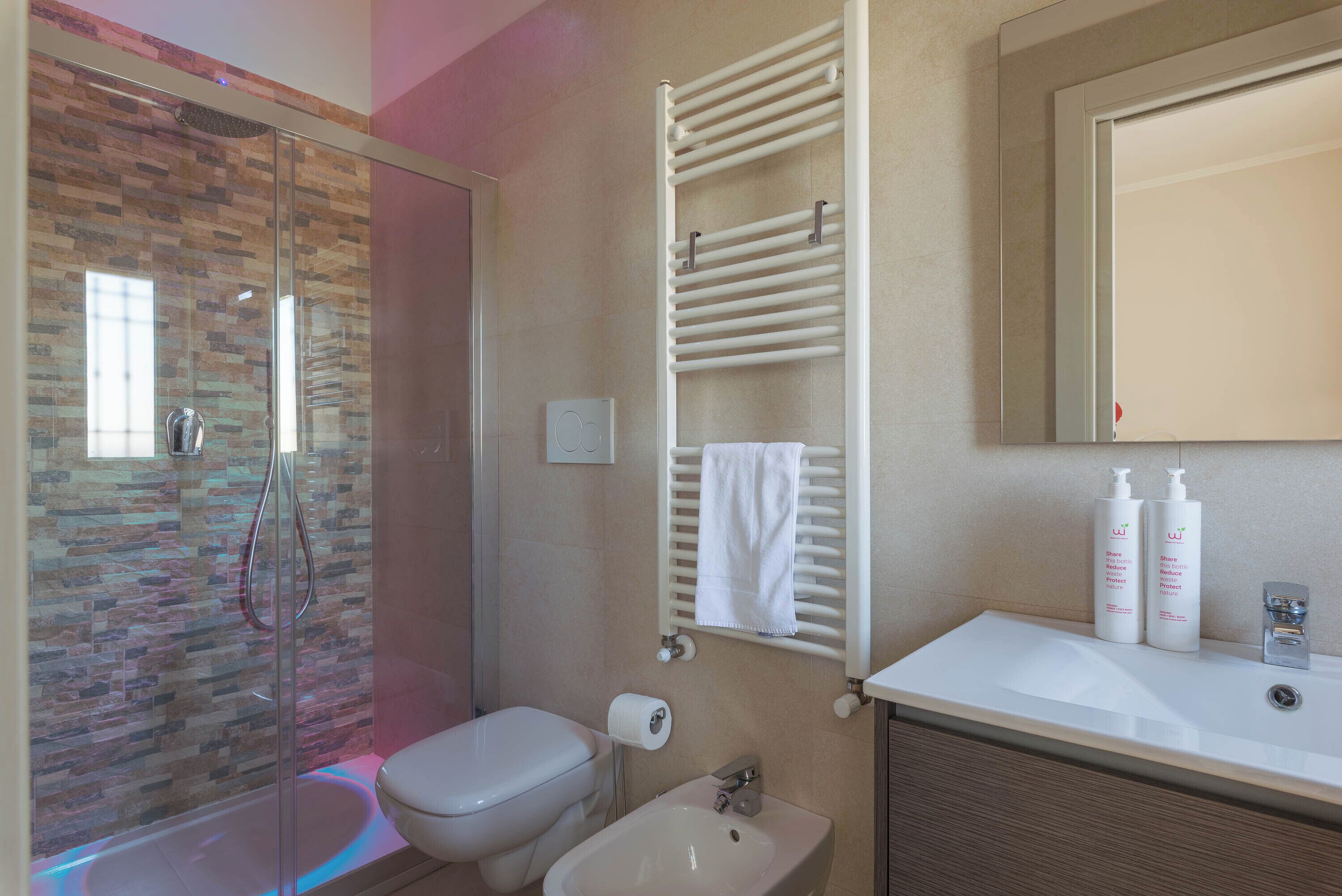 A bathroom with a glass shower enclosure, a toilet, a sink, and a towel rack.