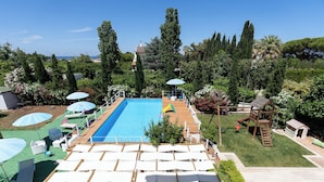 A swimming pool with a wooden deck, surrounded by lush greenery and a small playground. - Casa Torre Specchio (Bari)