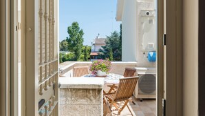 An open balcony with a table and chairs, a potted plant, and a view of a building and trees in the background. - Casa Torre Specchio (Bari)