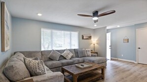 Un salon avec un canapé gris, une table basse en bois et un ventilateur de plafond.