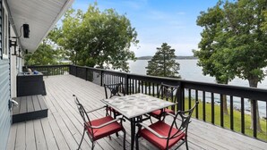 Une terrasse en bois avec une table et des chaises, donnant sur un lac bordé d’arbres.