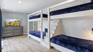 Une chambre avec des lits superposés, une commode grise et un tableau accroché au mur.
