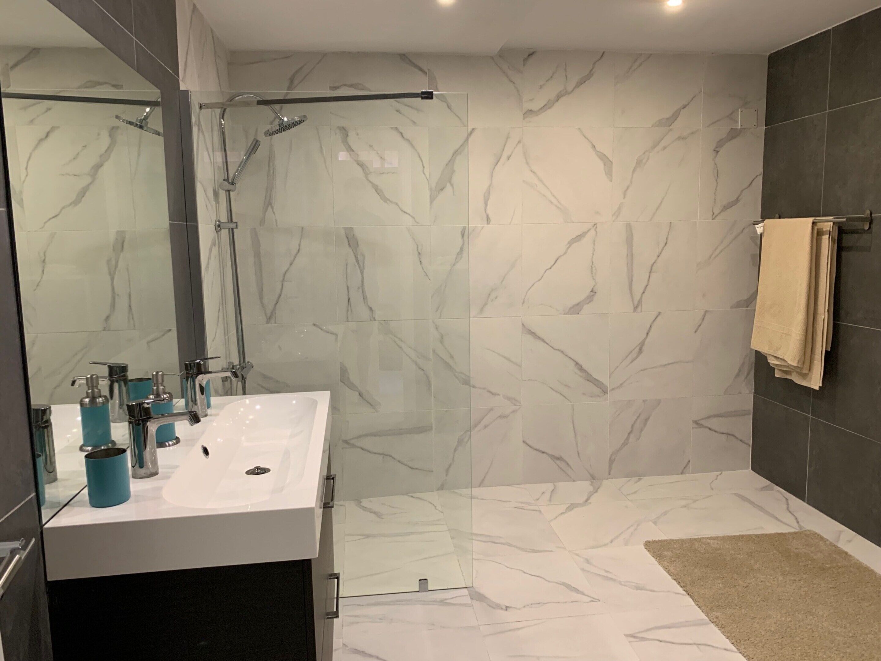 A modern bathroom with a glass-enclosed shower, a white sink with chrome fixtures, and marble-patterned walls.