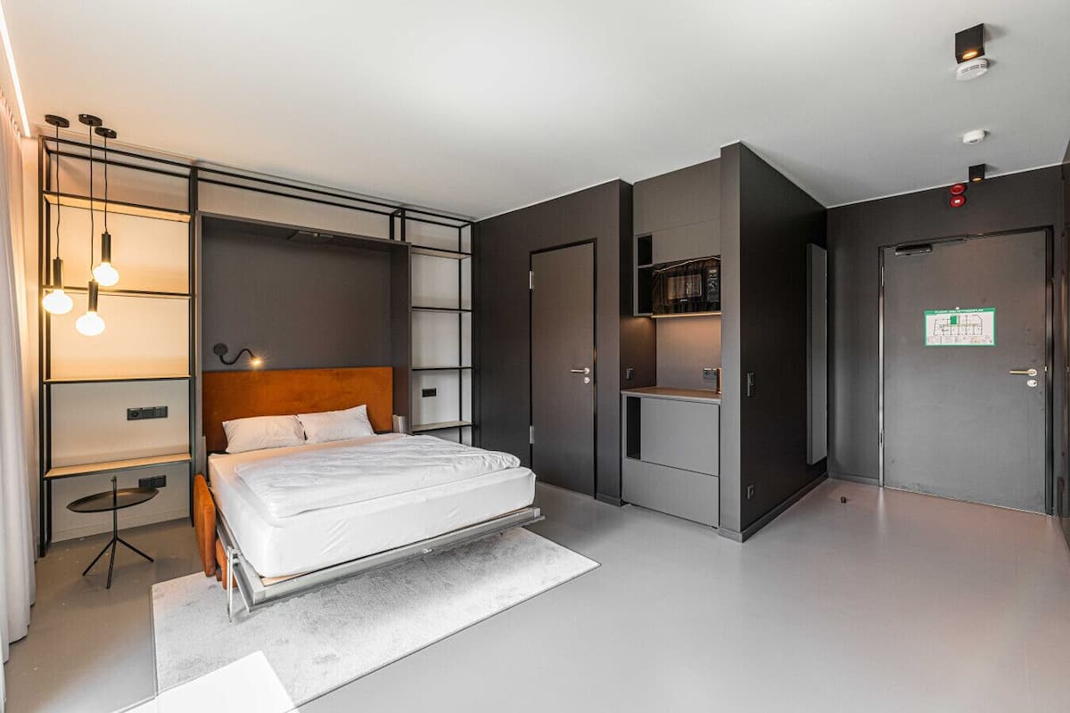A modern bedroom with a bed, built-in wardrobe, and a small kitchenette.