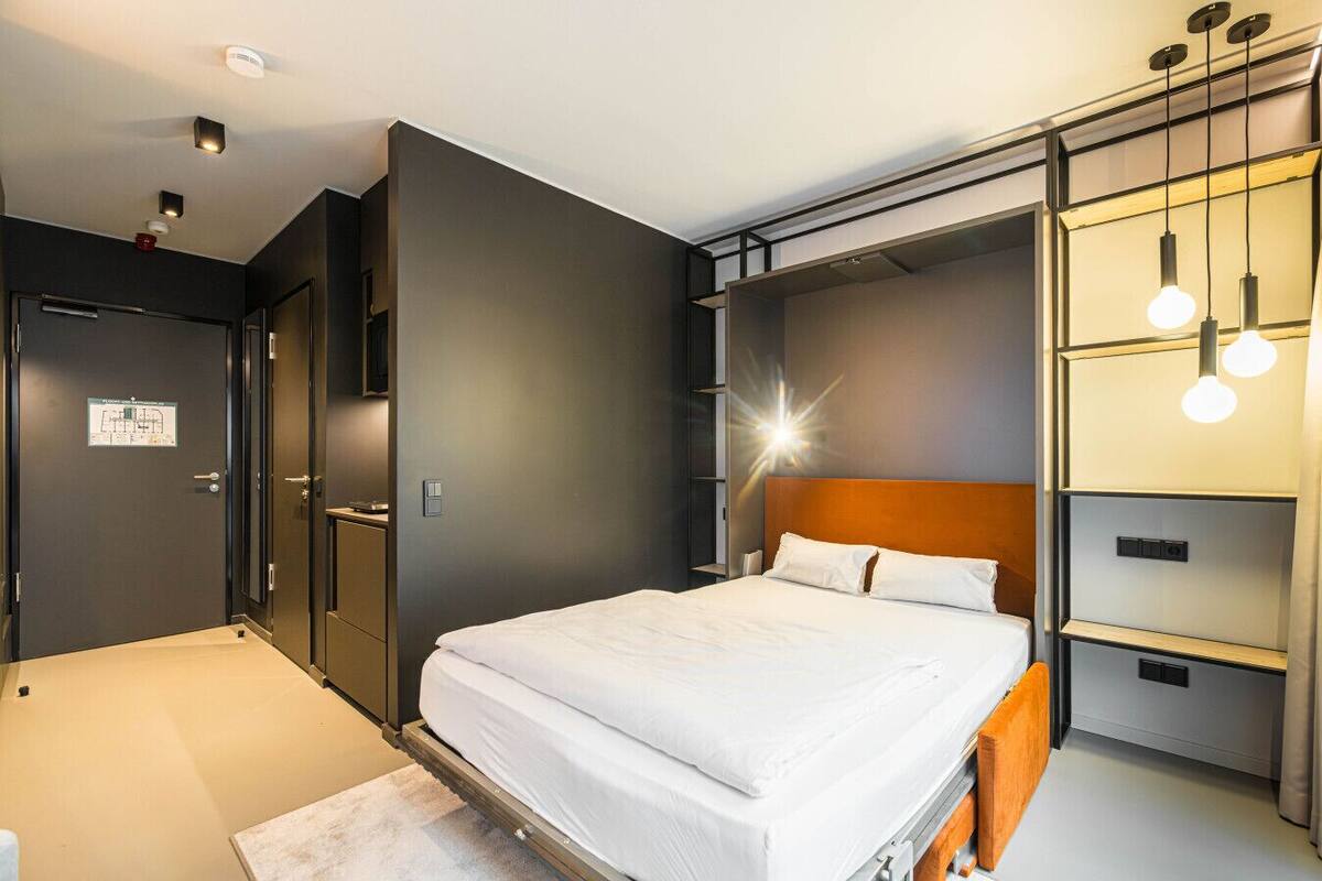 A modern hotel room with a bed, built-in wardrobe, and pendant lighting.