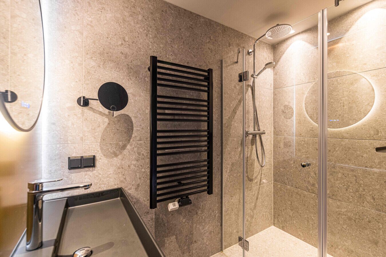 A modern bathroom with a glass shower enclosure, a black towel rack, and a wall-mounted control panel.