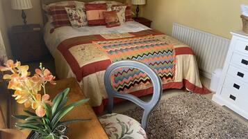 A bedroom with a bed, bedside tables, lamps, a chair, a small table with a plant, and a radiator.