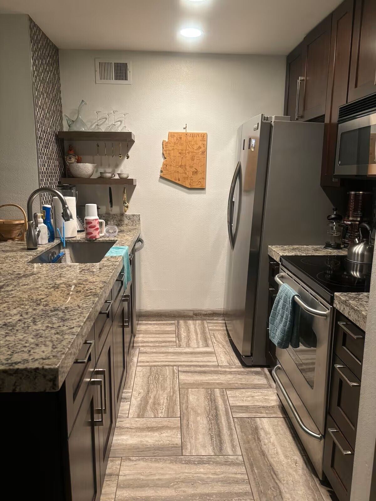 A kitchen with granite countertops, stainless steel appliances, and a herringbone wood floor.
