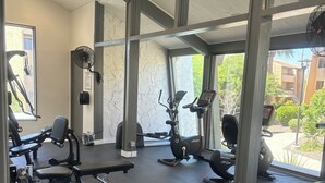 Een sportschool met trainingsapparatuur, grote ramen en een plafondventilator.