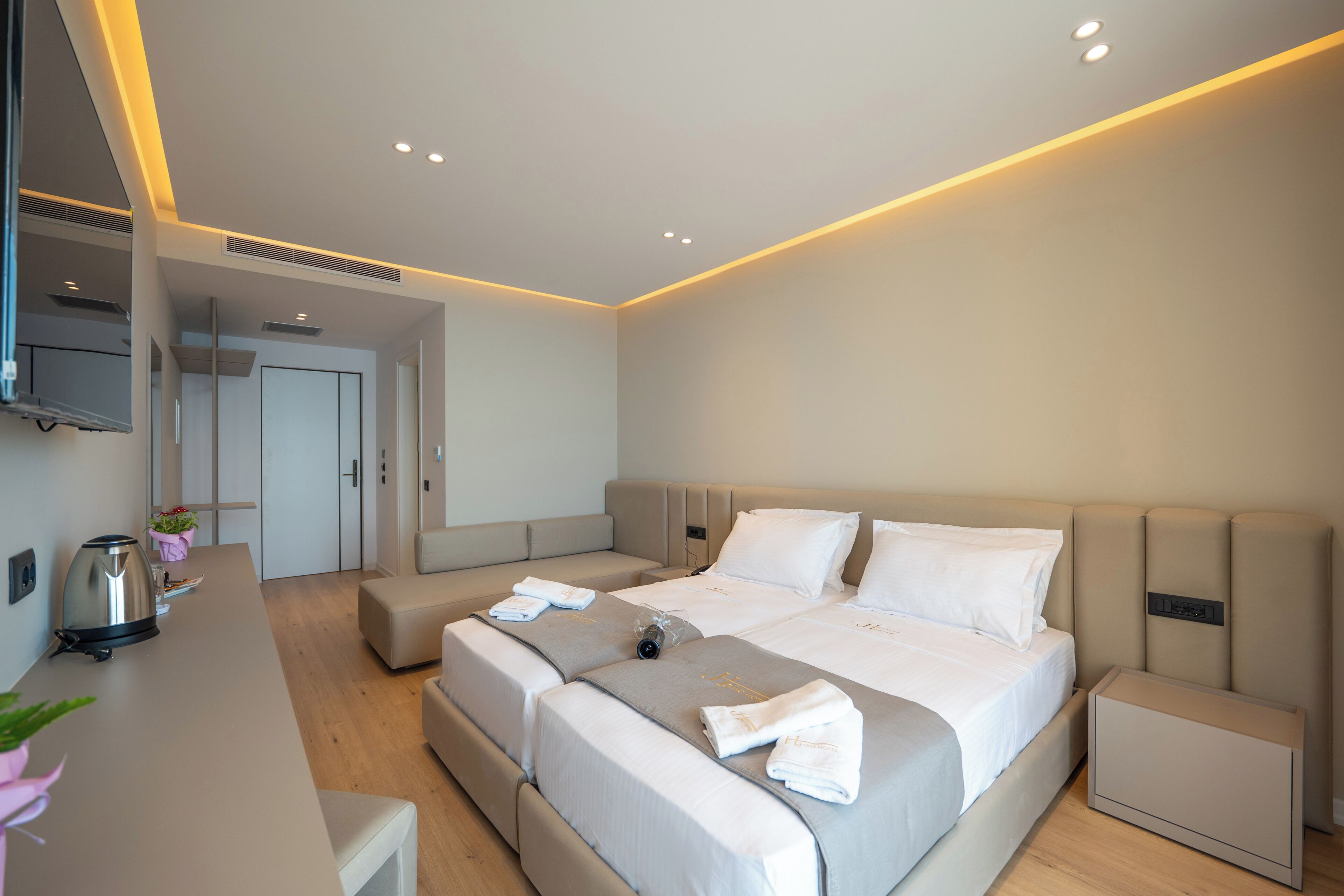 Une chambre d’hôtel moderne dotée d’un grand lit, de tables de chevet, d’un téléviseur à écran plat et d’un coin cuisine.