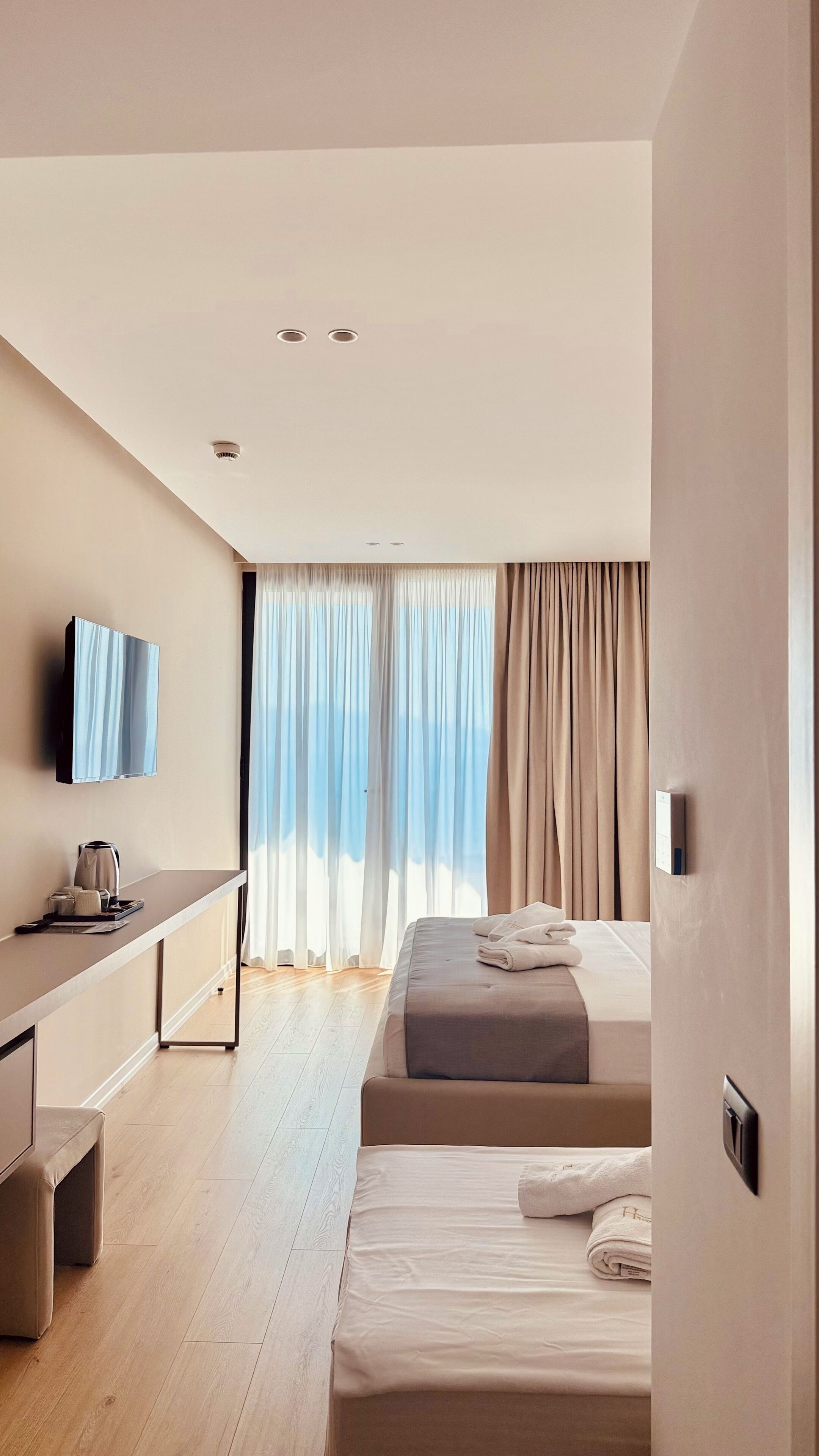 Ein modernes Hotelzimmer mit Bett, Schreibtisch, Fernseher und einem Fenster mit Vorhängen.