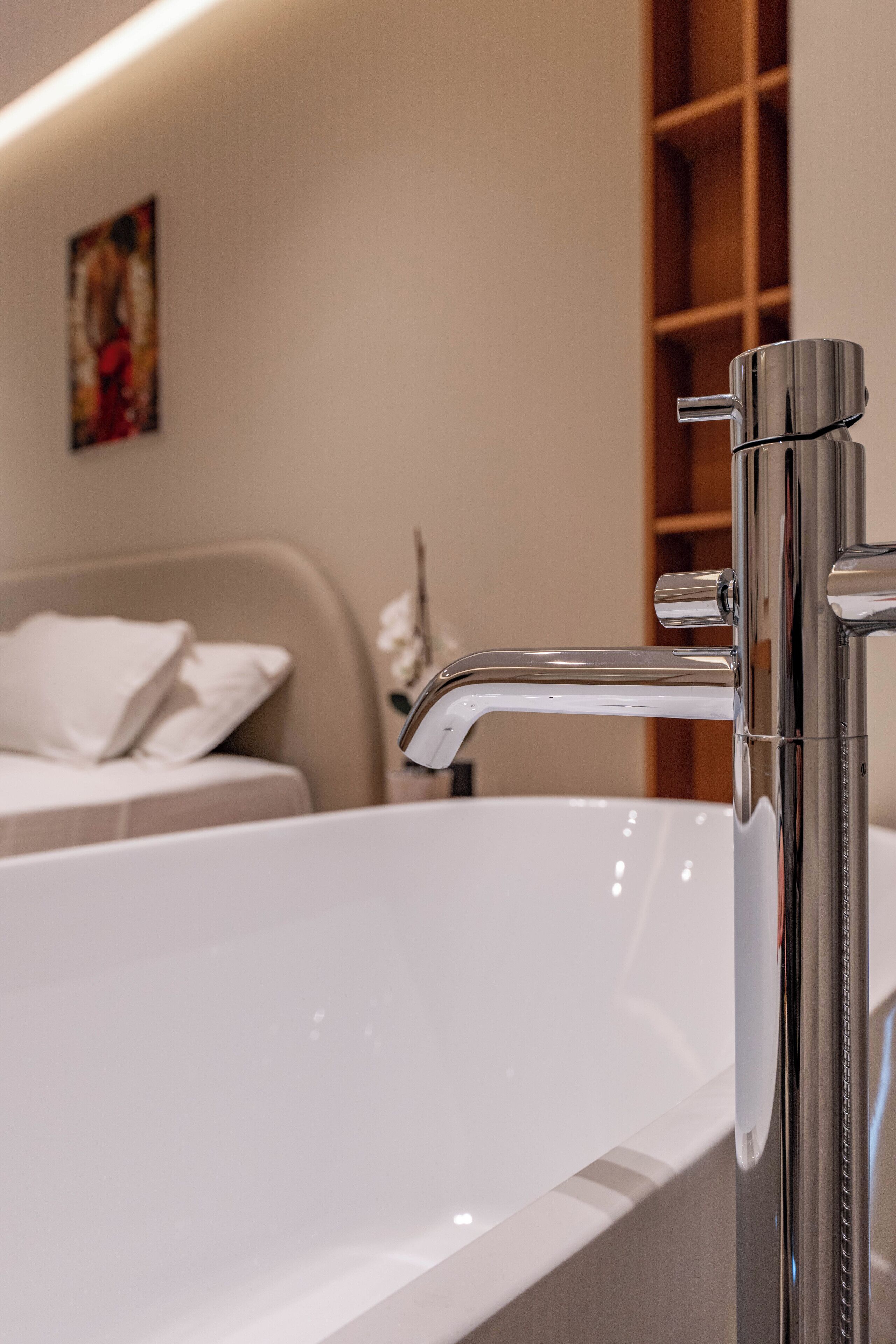 A modern bathroom with a chrome faucet, a white bathtub, and a wooden shelf in the background.
