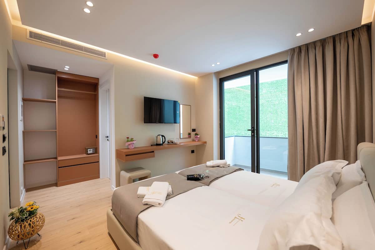 A modern hotel room with a large bed, a desk, a TV, and a balcony with curtains.
