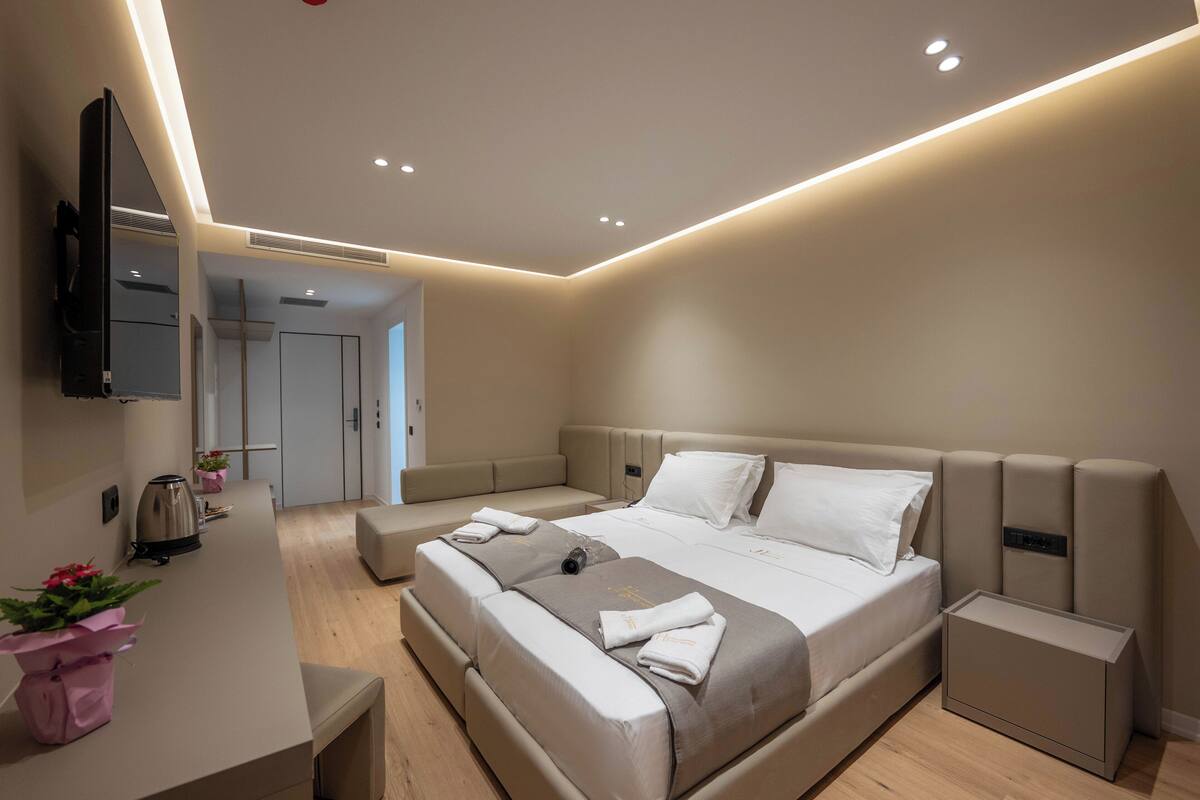 A modern bedroom with a large bed, bedside tables, a TV, and a bathroom in the background.