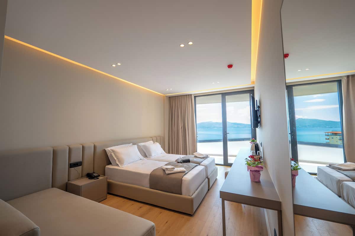 A modern hotel room with a large bed, a desk, and a view of the sea.