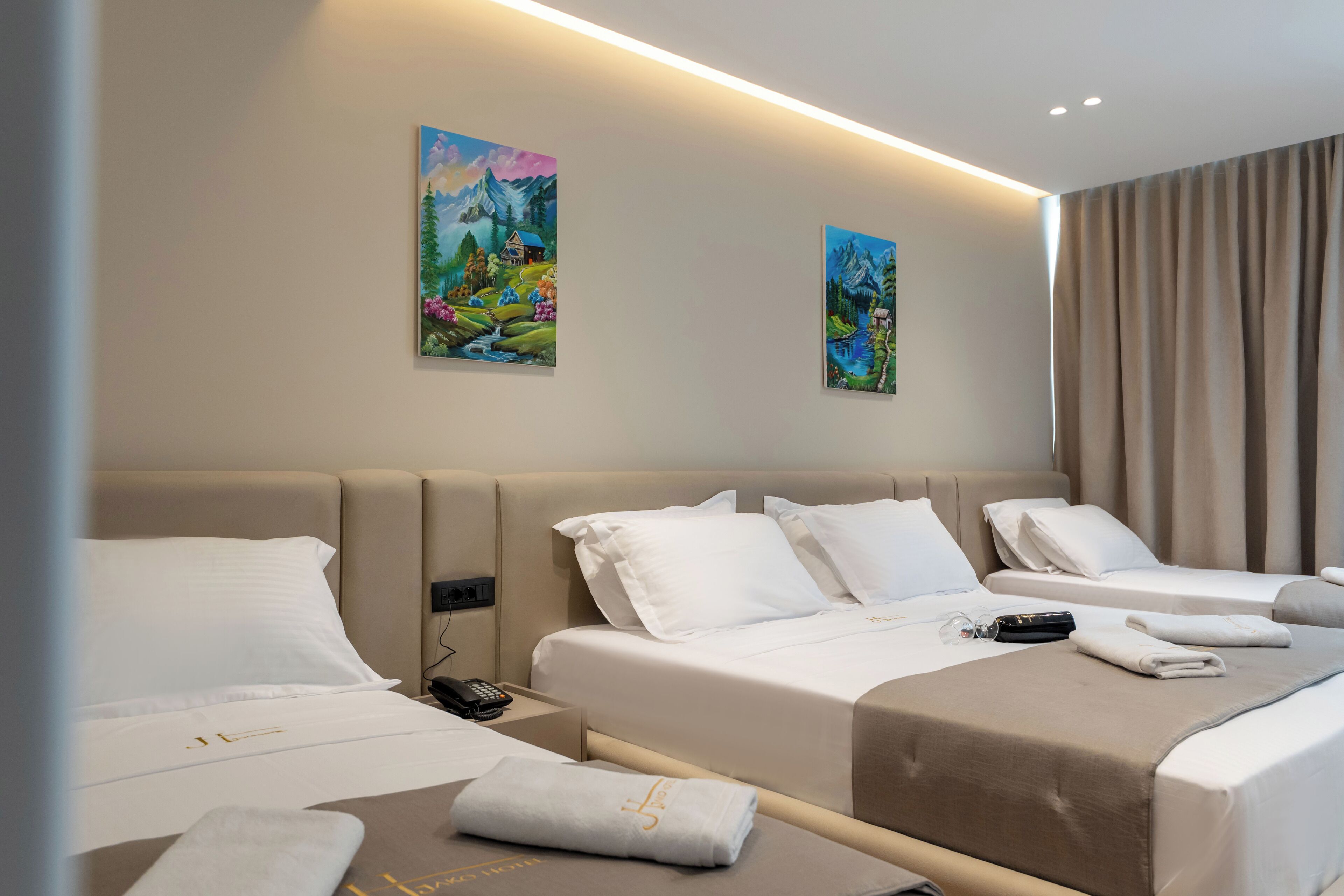 Una habitación de hotel con una cama grande, otra más pequeña, una mesita de noche con teléfono y obras de arte en las paredes.