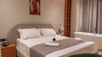 A hotel room with a bed, a telephone, a painting on the wall, a bathroom with a bathtub, and a curtain.
