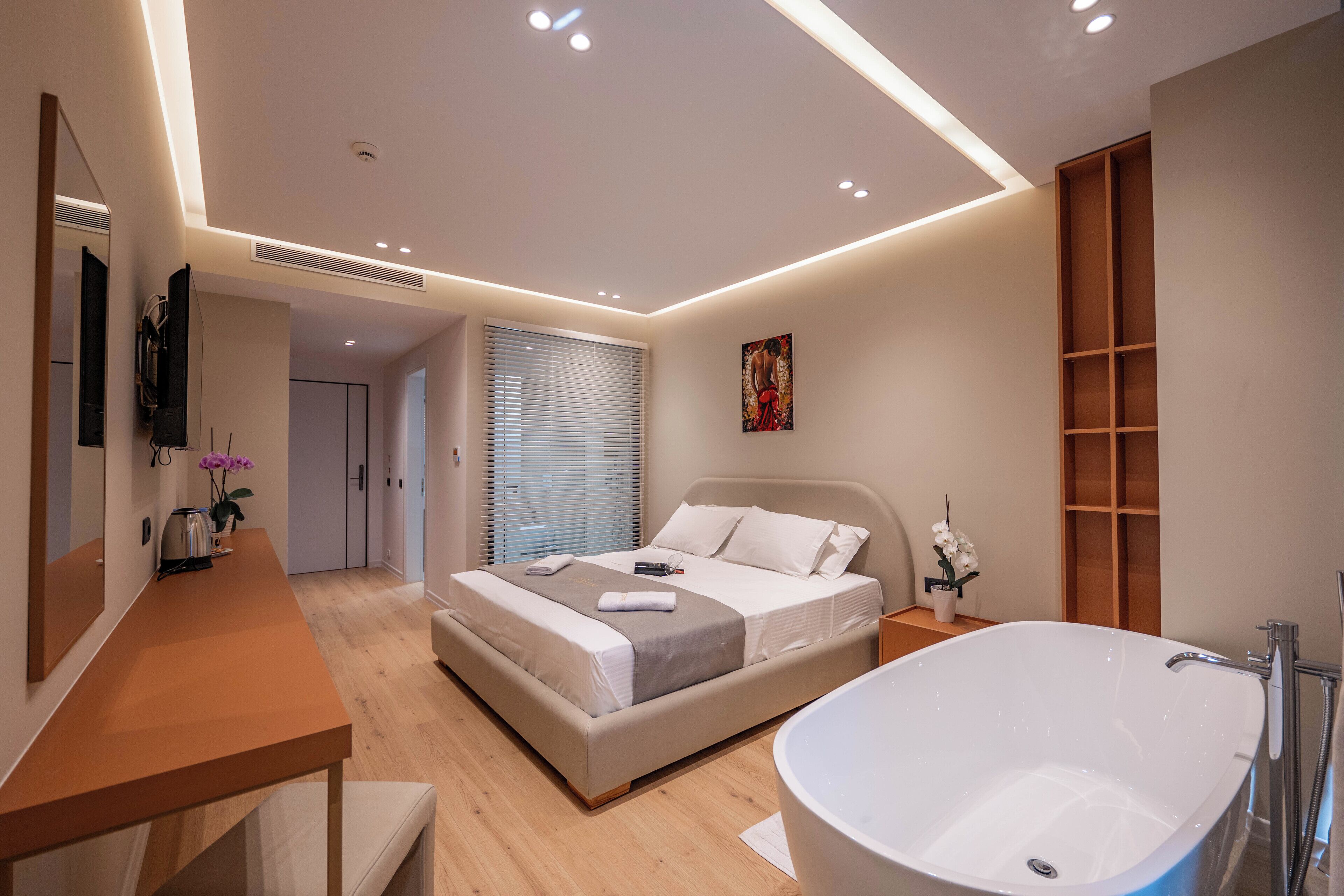 A modern bedroom with a large bed, a vanity with a mirror, a bathtub, and a wooden shelf unit.
