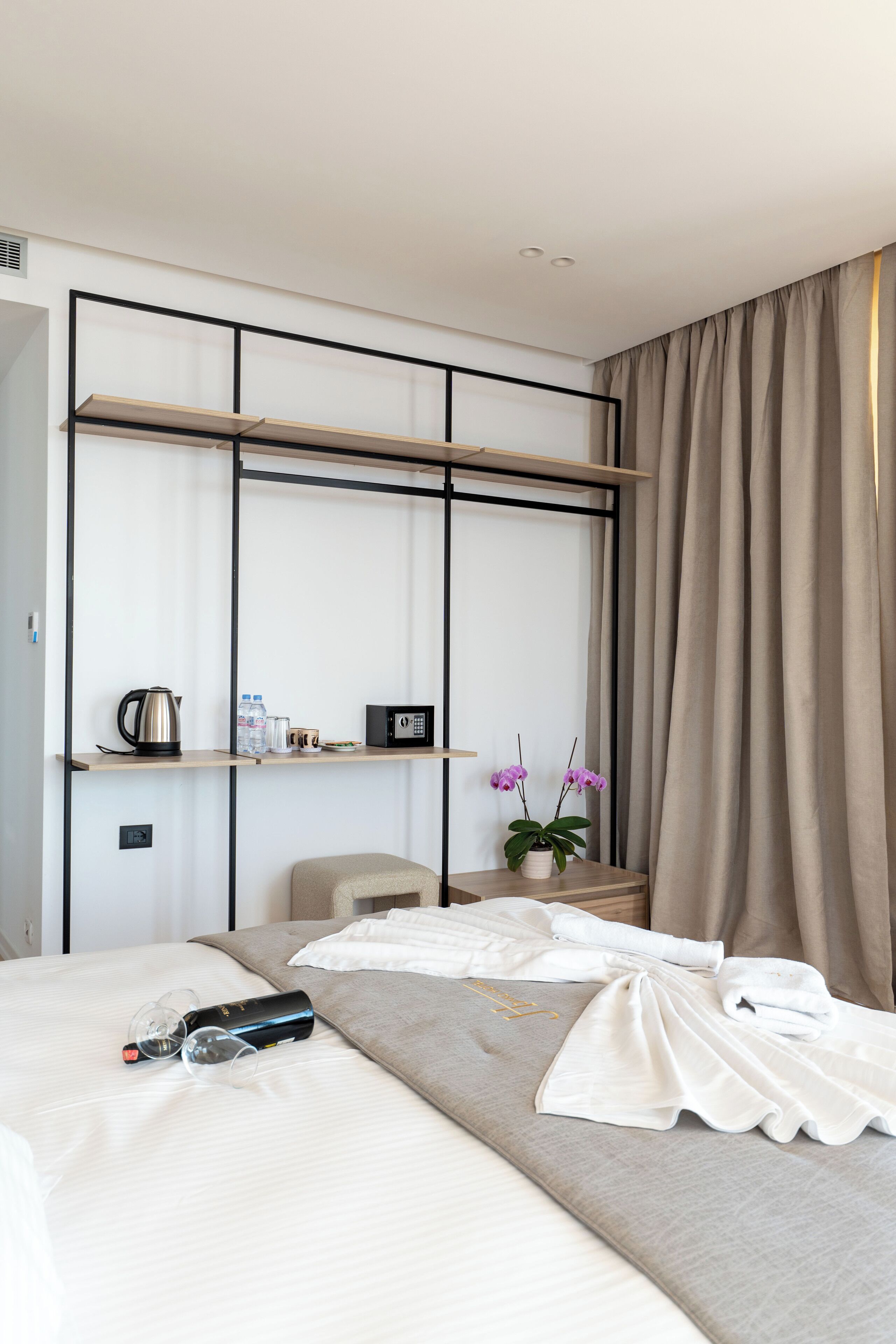 A hotel room with a bed, a bedside table with a kettle, a microwave, and a potted plant.