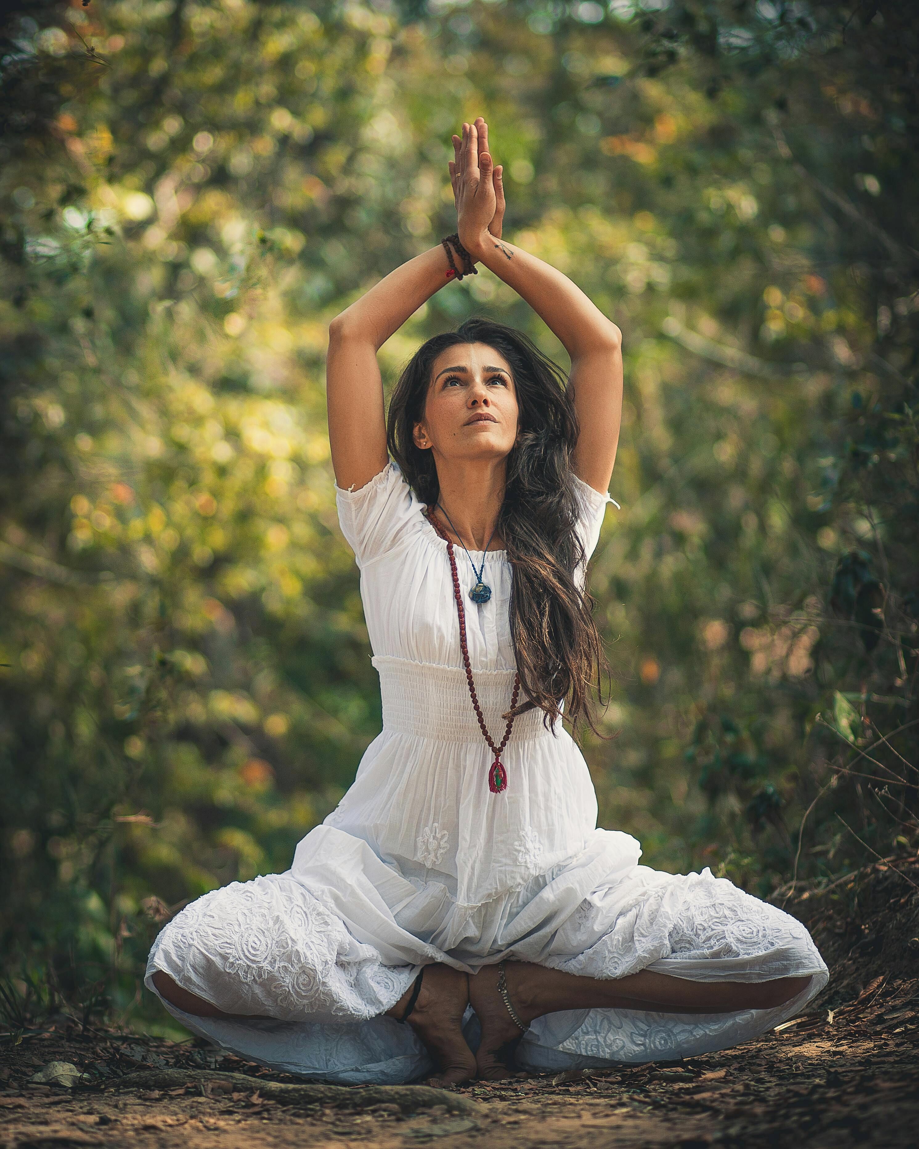 A person in a white dress sitting in a meditative pose outdoors.