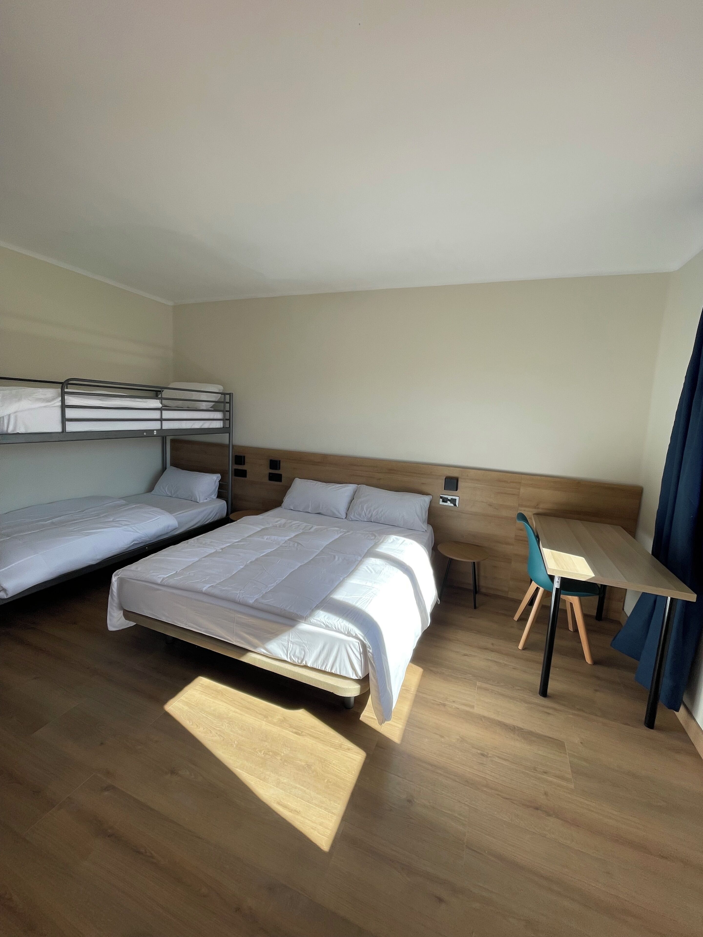 Una habitación de hotel con dos camas individuales, un escritorio de madera, una silla y una mesita.