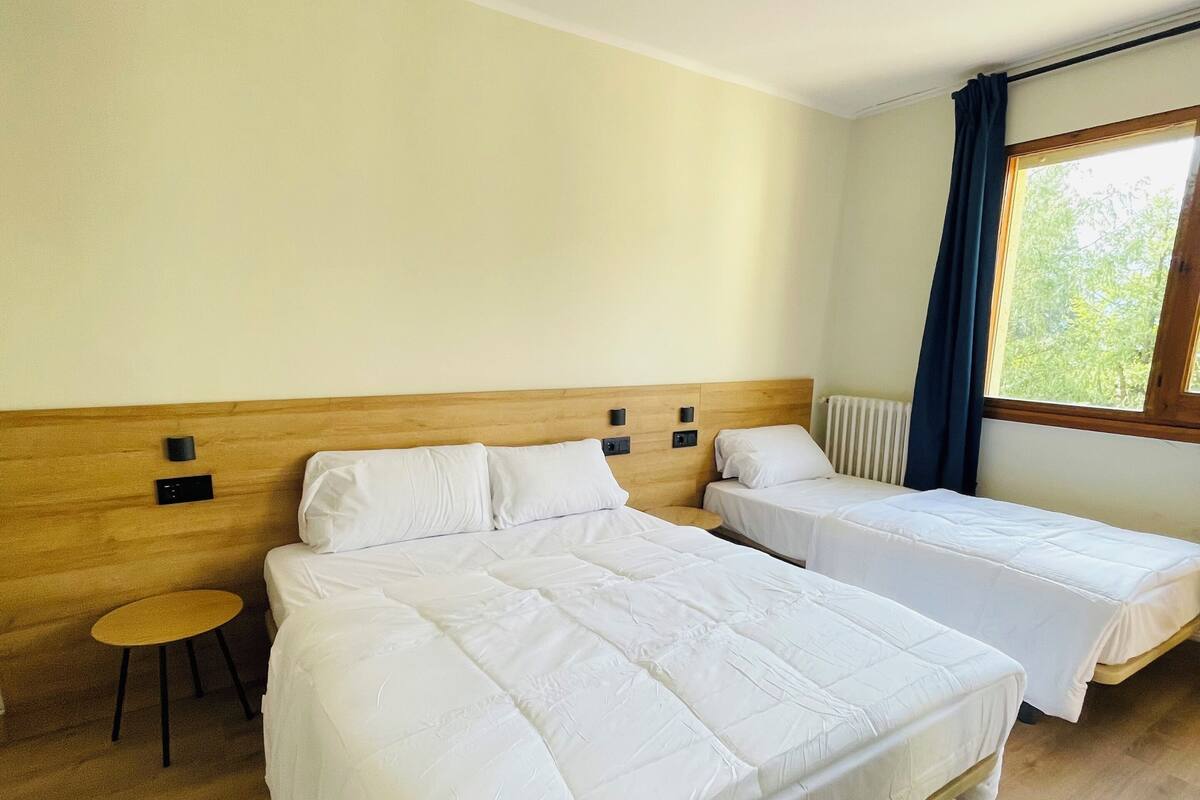 Una habitación de hotel con dos camas, una mesita redonda y una ventana con cortinas.