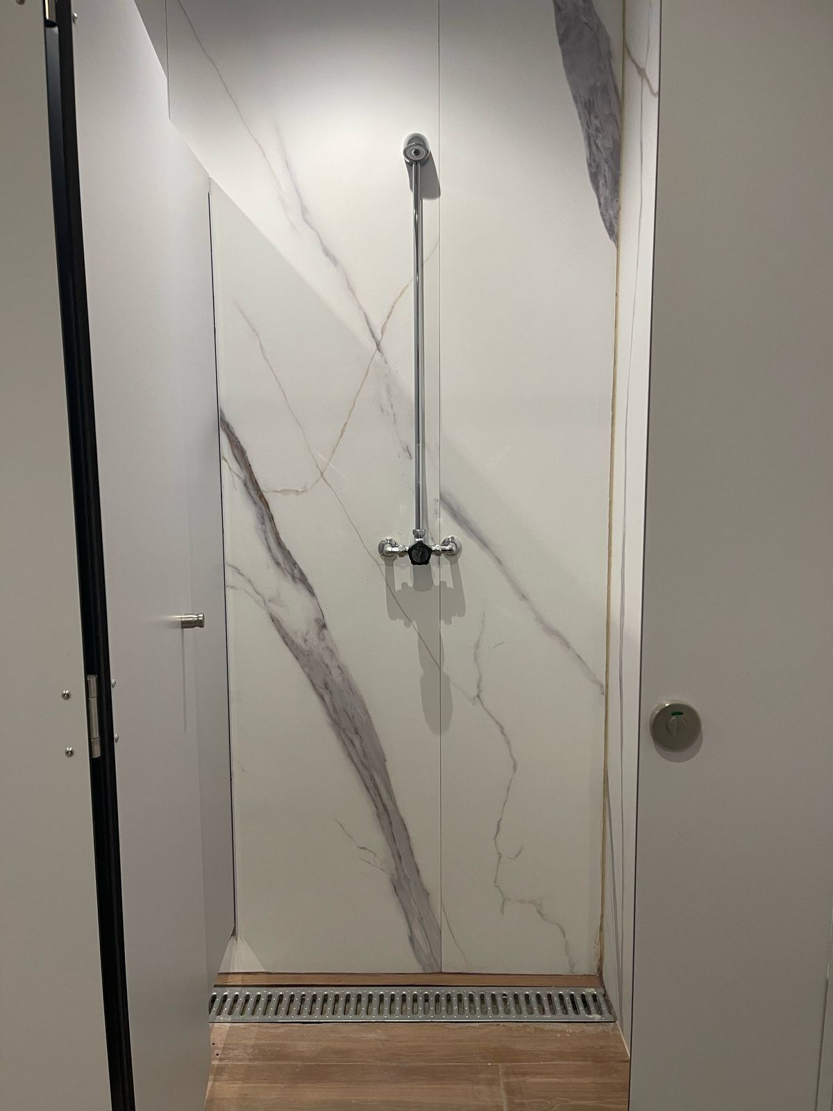 A shower with a marble wall and a wooden floor.