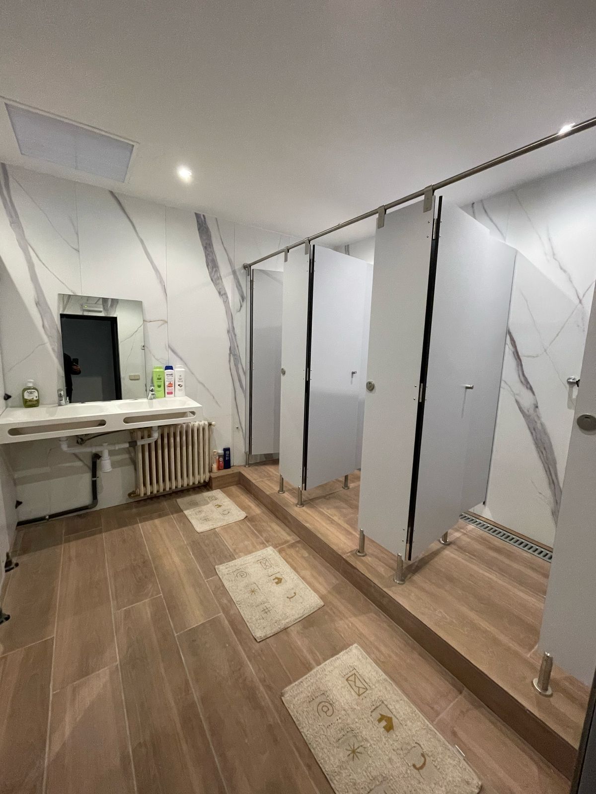 Un baño moderno con paredes de mármol, tocador con artículos de aseo y zona de ducha.