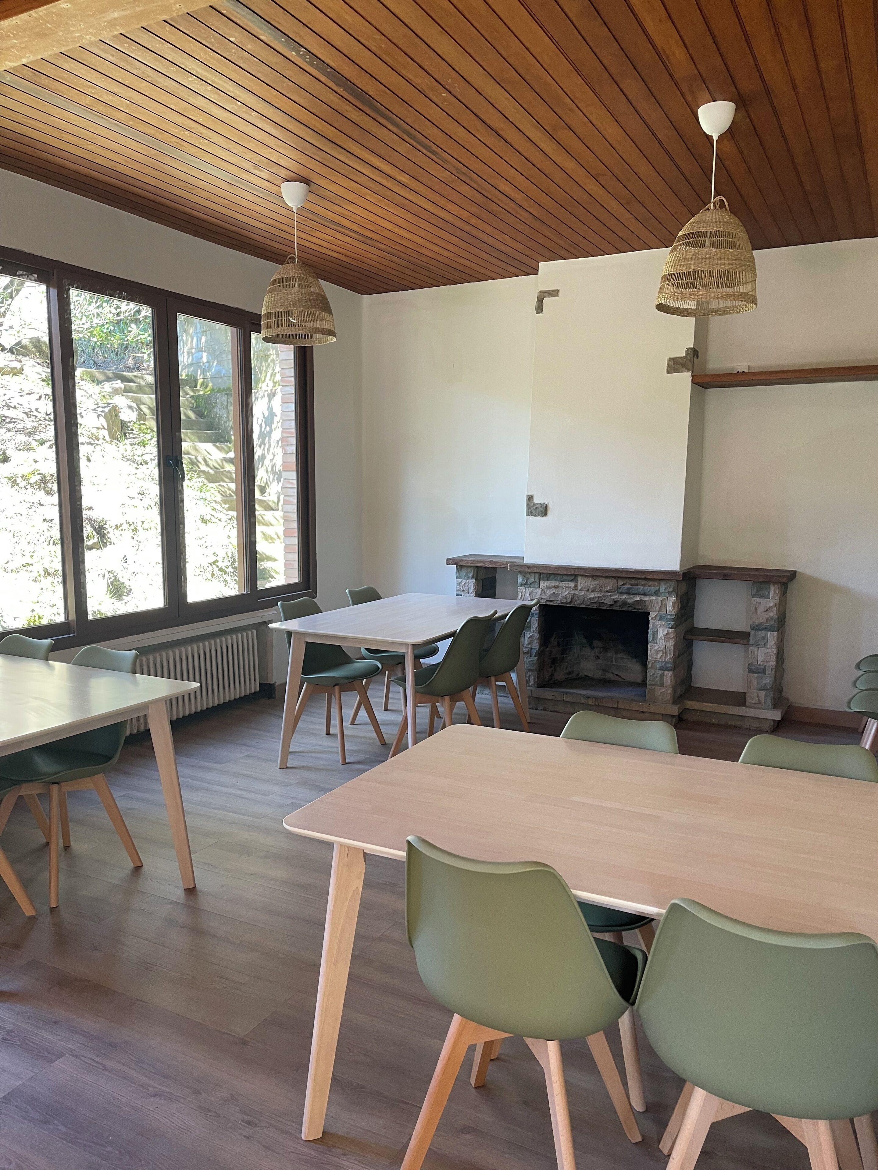 A dining area with wooden tables and chairs, a stone fireplace, and large windows.