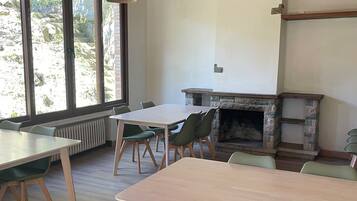 A dining area with wooden tables and chairs, a stone fireplace, and large windows.