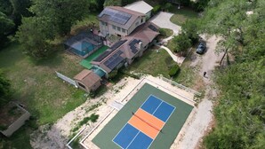 Vista aèria d'una zona residencial amb una pista de tennis, una casa amb panells solars i un jardí tancat.