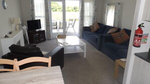 A living room with a sofa, a coffee table, a TV, and a fireplace. - Cosy 3 Bedroom Lodge at Avonvale Holiday Park (Evesham)