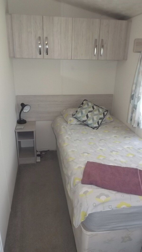 A small, neatly arranged bedroom with a single bed, a bedside table with a lamp, and a wardrobe with two doors.