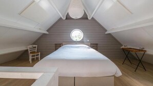 Ein Schlafzimmer im Dachgeschoss mit hohen Decken, einem großen Bett, einem kleinen Tisch und einem Stuhl.