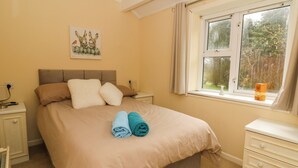 Un dormitorio con cama, mesitas de noche, una ventana con vistas a árboles y un cuadro en la pared.