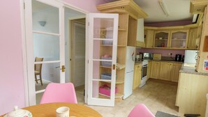 Una cocina con armarios de madera, una mesa de comedor con sillas rosas y un refrigerador.