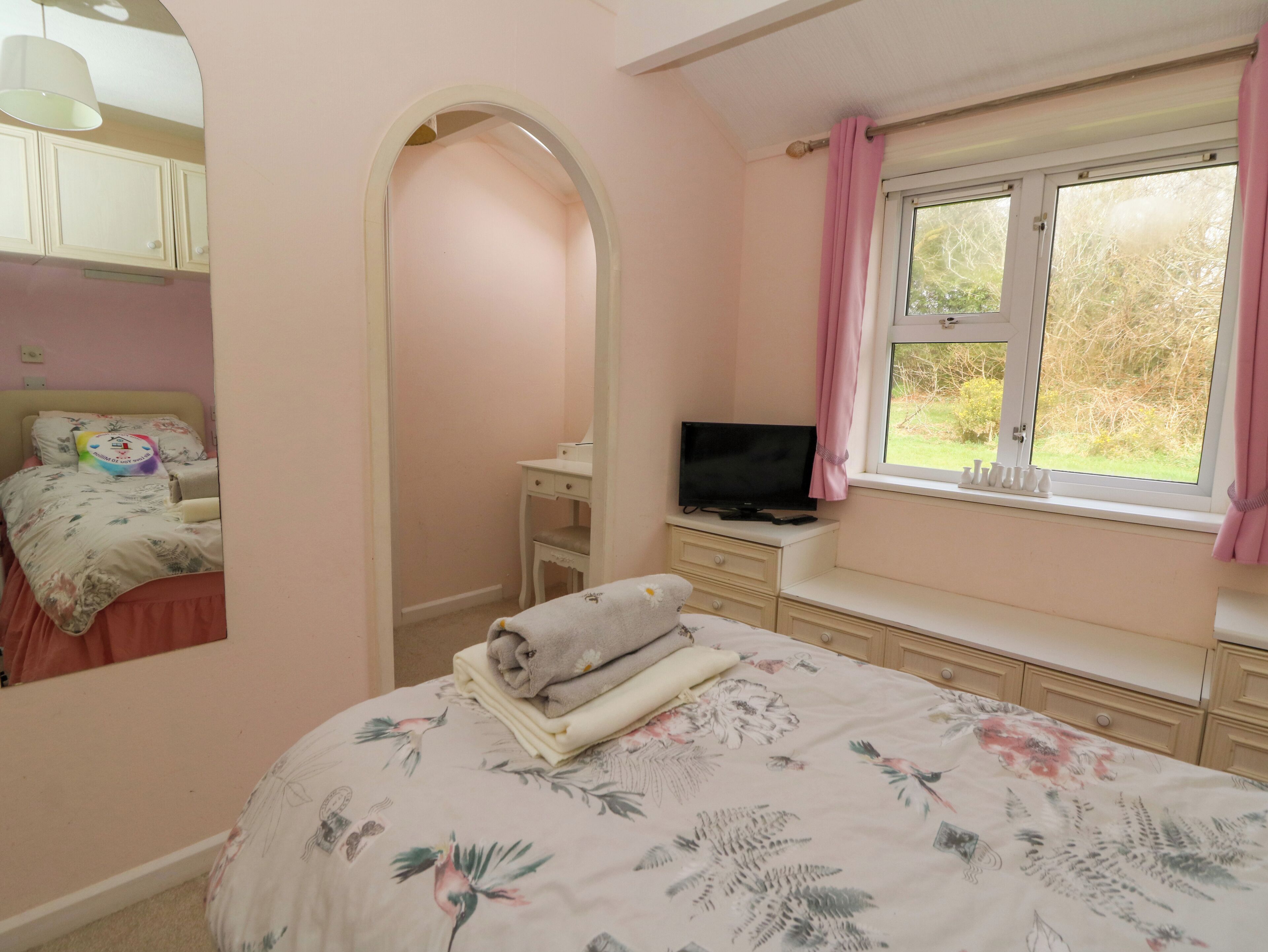 A bedroom with a bed, a TV, a window with curtains, a dresser, and a mirror.