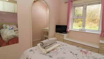 A bedroom with a bed, a TV, a window with curtains, a dresser, and a mirror.