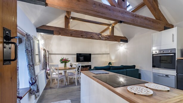A modern kitchen with wooden beams, a dining area with a table and chairs, and a cozy seating area with a green sofa. - The Stables at Brambles Farm - Sleeps 2, Wifi (Leek)
