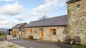 A stone building with a paved driveway and a small outdoor seating area with two wooden chairs and a table. - The Stables at Brambles Farm - Sleeps 2, Wifi (Leek)