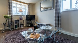 A modern living room with a glass coffee table, a sofa, a TV, and a bookshelf.
