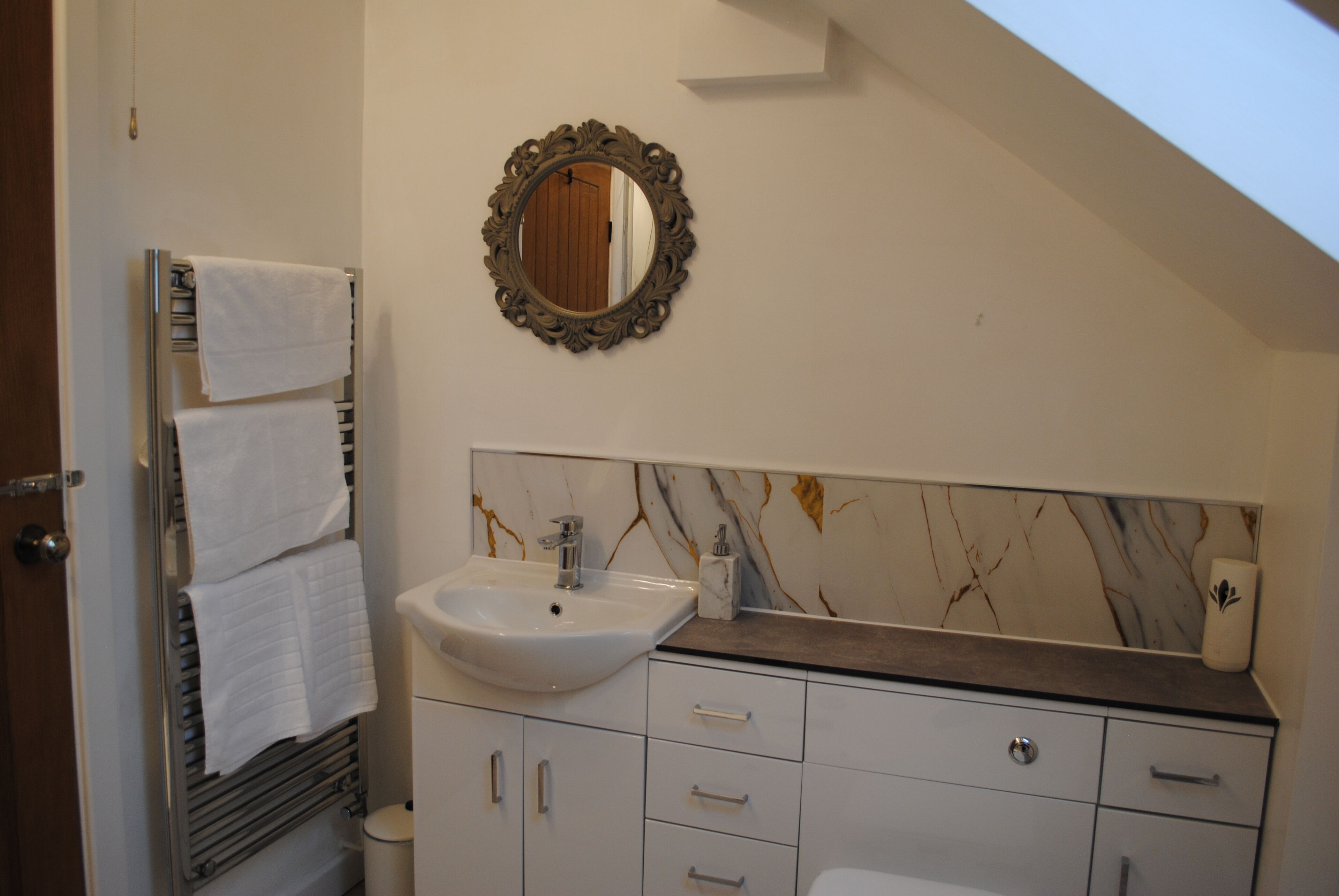 A bathroom with a white sink, a mirror with an ornate frame, and a towel rack with multiple towels.