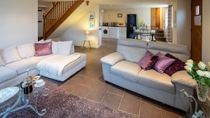A spacious living area with two sofas, a coffee table, and a rug. A staircase leads to a kitchen area with a washing machine and a dining table.
