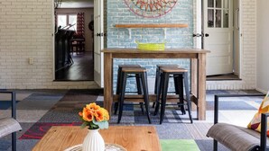 A living room with a wooden coffee table, a white vase with flowers, a blue and white brick wall, a wooden bench, and a door with glass panels. - Stylish home in Little Rock (Little Rock)