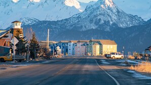 A town with colorful buildings, a road, and snow-covered mountains in the background.