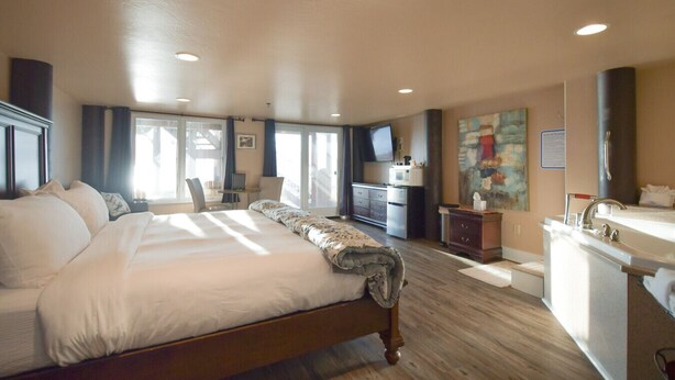 A spacious bedroom with a large bed, a desk, a television, and a bathroom with a sink and mirror.